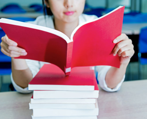 young woman reading a red book on a stack of other red books
